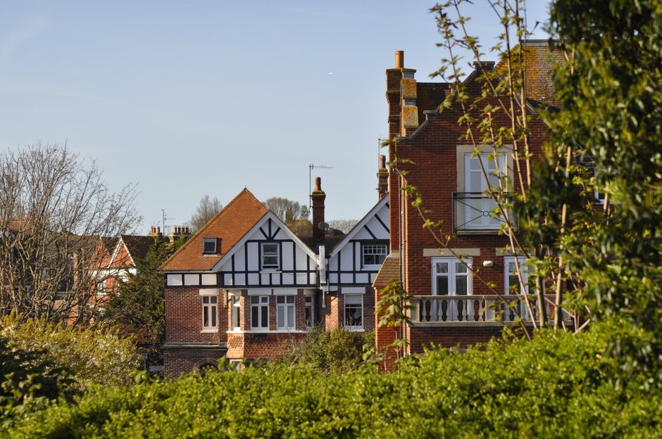 A row of traditional British residential buildings featuring red brick exteriors and pitched roofs, with one building displaying distinctive black-and-white Tudor-style timber framing. The homes are p